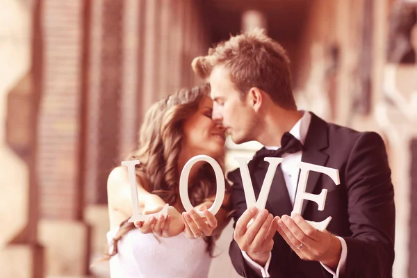 Beautiful bride and groom kissing and holding LOVE letters — Stock Photo, Image