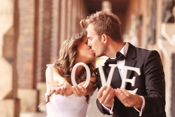 Beautiful bride and groom kissing and holding LOVE letters — Stock Photo, Image