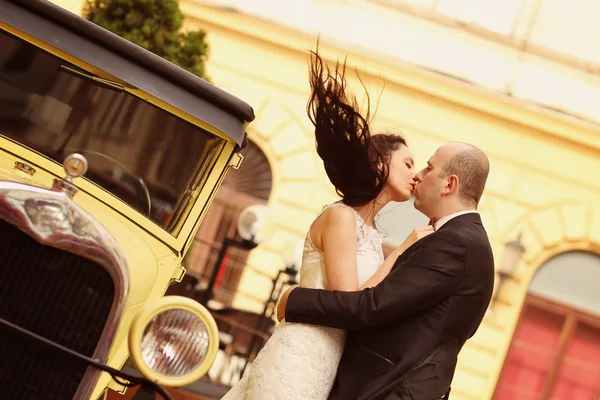 Krásná nevěsta a ženich všeobjímající poblíž klasické auto — Stock fotografie