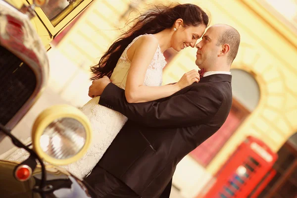 Όμορφη νύφη και γαμπρός αγκαλιάζοντας κοντά κλασικό αυτοκίνητο — Φωτογραφία Αρχείου