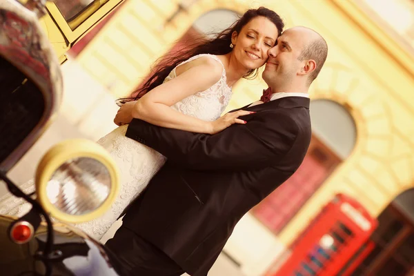 Beautiful bride and groom embracing near classic car — Stock Photo, Image