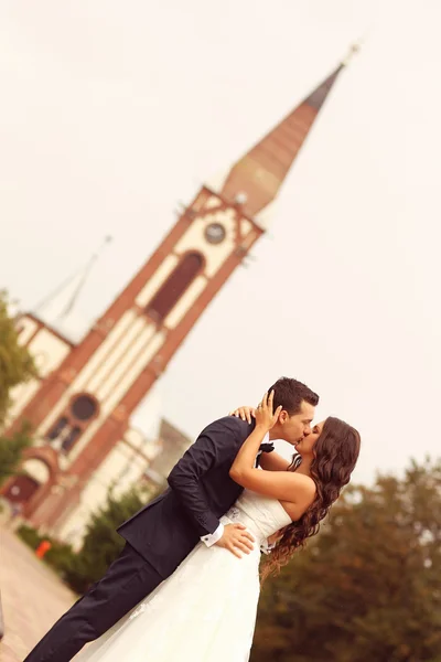 Beautiful bride and groom embracing near church — Stock Photo, Image