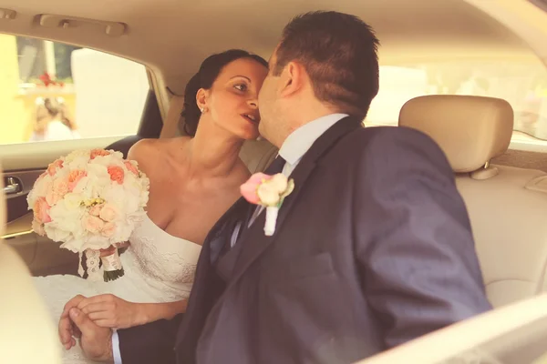 Hermosa pareja de novias besándose en el asiento trasero de un coche — Foto de Stock