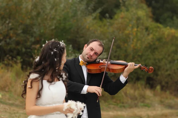 Bella sposa e sposo divertirsi con le piume nel parco con lo sposo che suona al violino — Foto Stock