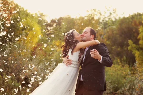 Schöne Braut und Bräutigam haben Spaß mit Federn im Park — Stockfoto
