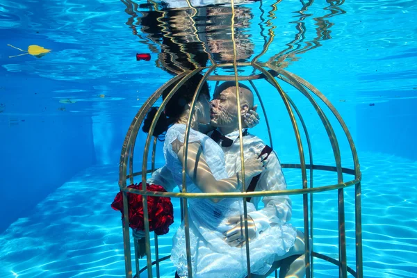 Красивые невеста и жених веселятся под водой в клетке для птиц — стоковое фото