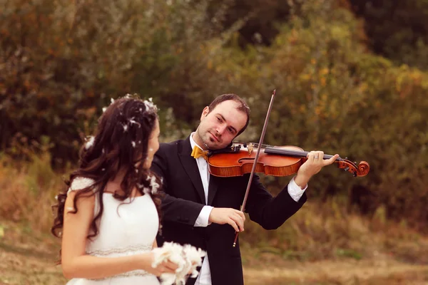 Beautiful bride and groom having fun with feathers in park with groom playing at violin Royalty Free Stock Photos