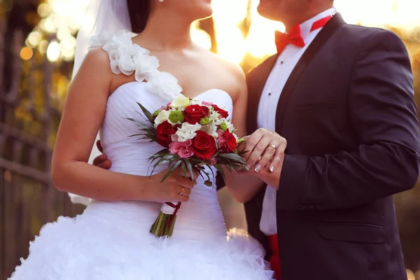 Beautiful bride and groom embracing and holding flower bouquet — Stock Photo, Image