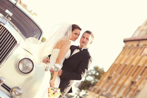 Hermosa novia y novio abrazando cerca de coche clásico en la ciudad —  Fotos de Stock