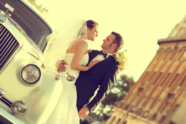 Hermosa novia y novio abrazando cerca de coche clásico en la ciudad —  Fotos de Stock