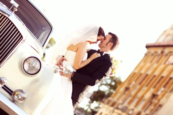 Hermosa novia y novio abrazando cerca de coche clásico en la ciudad —  Fotos de Stock