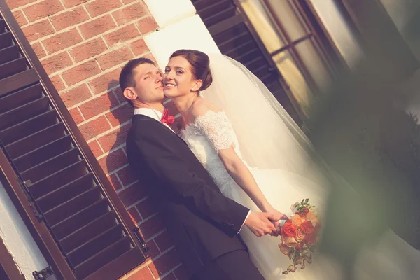 Beautiful bride and groom embracing near brick building — Stock Photo, Image