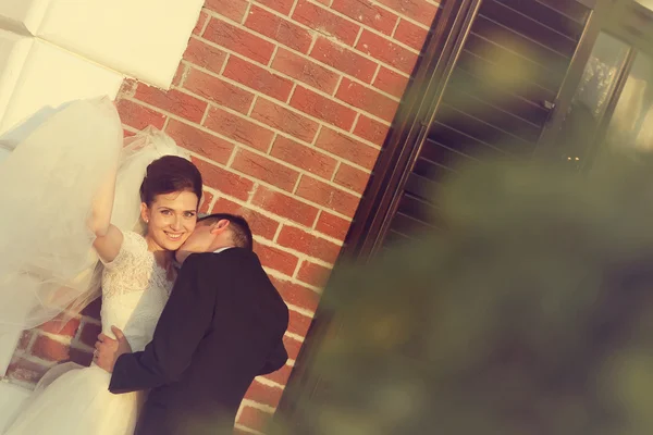 Beautiful bride and groom embracing near brick building — Stock Photo, Image