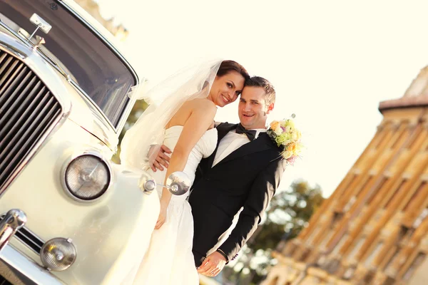 Krásná nevěsta a ženich všeobjímající poblíž klasické auto v městě Stock Snímky