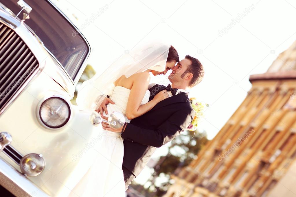 Beautiful bride and groom embracing near classic car in city