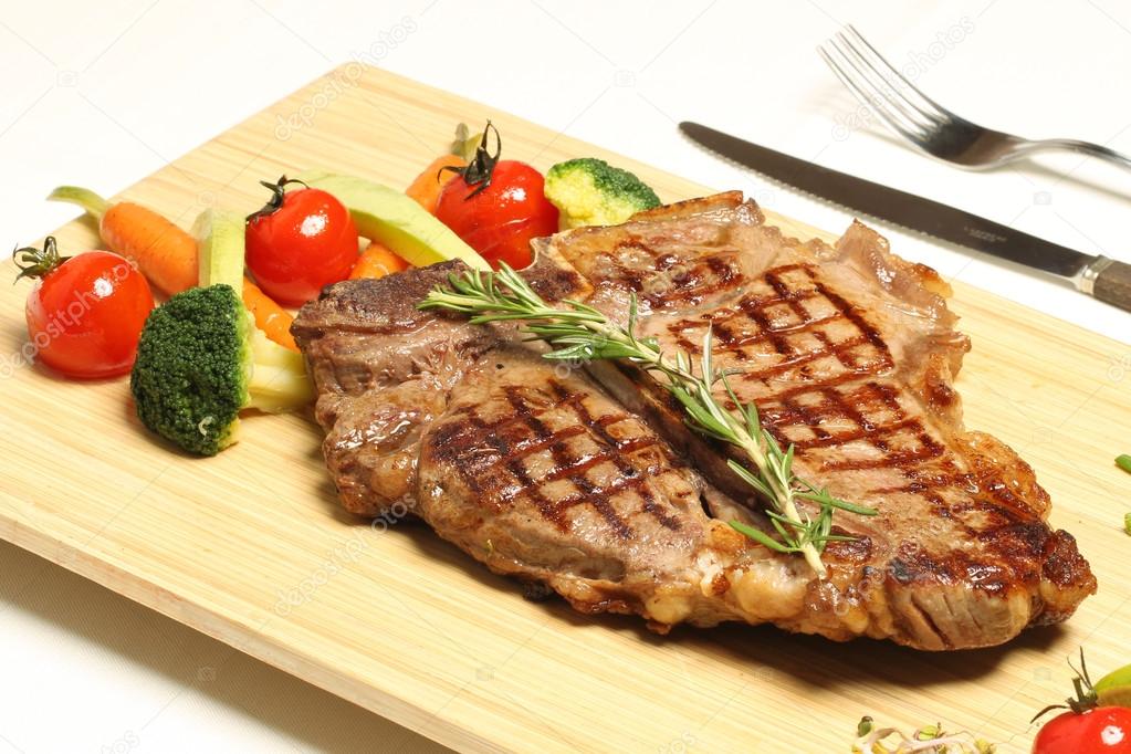Succulent thick juicy portions of grilled fillet steak served with tomatoes and roast vegetables on an wooden board