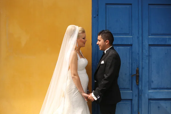 Beautiful bride and groom holding hands next to colorful door and wall — Stock Photo, Image