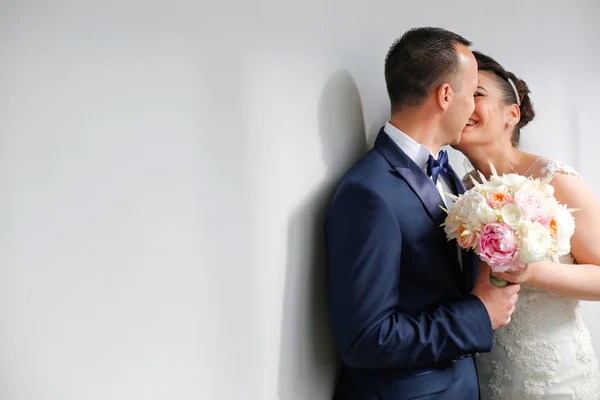 Casal de noiva bonita beijando ao lado de parede branca — Fotografia de Stock