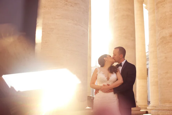 Beautiful bridal couple embracing and kissing near columns — Stock Photo, Image