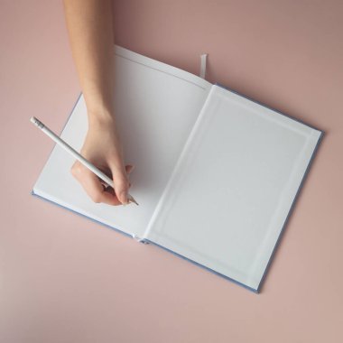 El deftere yazmaya başlar. Pastel arka planda saf beyaz kağıt.