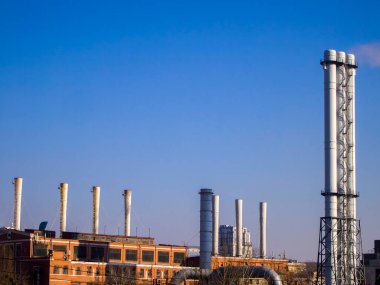 Mavi arka planda gri fabrika bacaları. Sadece bir borudan dumanlar yükselir ve diğerleri geçici olarak çalışmaz. Endüstriyel arazi. Ekoloji kavramı.