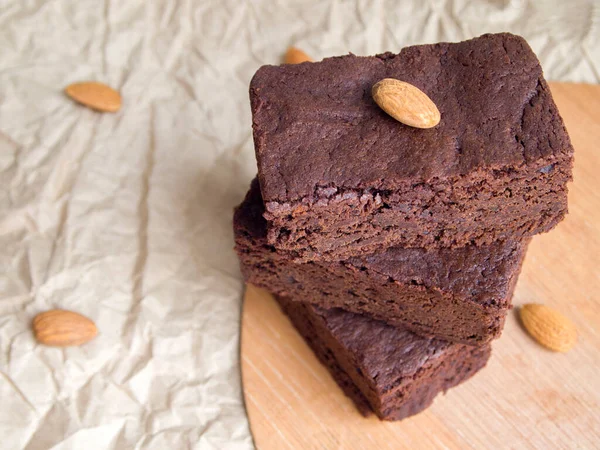 Ahşap tezgahta ve buruşuk el işi kağıdında nefis siyah çikolatalı brownie. Tarafsız ışık arka planında badem fıstığıyla süslenmiş iştah açıcı köy pastası. Lezzetli ve ev yapımı tatlı hazırlamak kolay.