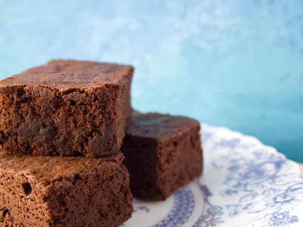Açık mavi arka planda mavi desenli güzel bir tabakta üç lezzetli browni dilimi. Çikolatalı pasta iştah açıcı. Boşluğu kopyala.