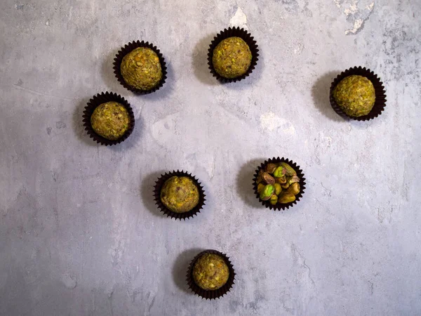 Some pistachio truffles in a brown candy wrapper on the gray concrete background. In one of the wrappers instead of candy are nuts (pistachios).