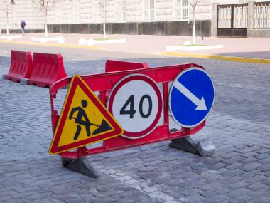 Kaldırımın bir kısmı kırmızı plastik bariyerler tarafından kapatılmış. Uyarı levhası 