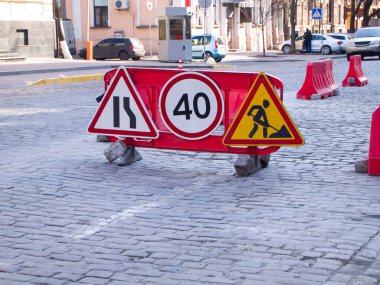 Yolun bir kısmı onarılıyor. Araba yolu kırmızı plastik bariyerler tarafından kapatıldı. Üç yol işareti var, tamirat uyarısı ve sorun bölgesinde nasıl araba kullanılacağını gösteriyor.