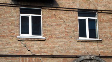 Evin üzerinde derin çatlaklar görünmeye başladı. Eski bina çökmeye başlıyor. Modern plastik pencereli tuğla bir evin duvarı.