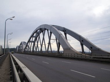 Bir karayolu parçası kemerli bir demiryolu köprüsü ile birleştirilmiş. Bulutlu bir günde köprüde hiç yaya yoktur, arabalar uzaktan görülebilir..