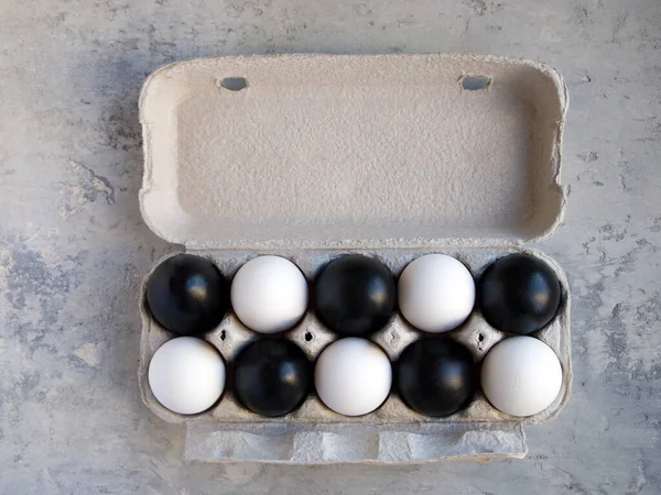 Carton packaging for eggs filled with white and black eggs. Half of the eggs are painted black, half has a natural white color. Ideas for Easter. Copy space. You can write text on the top of box