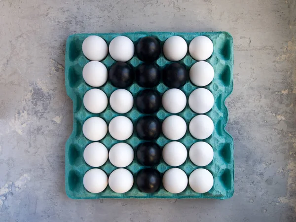 Tavuk yumurtalı büyük karton tepsi. Bazıları siyah, bazıları da beyaz. Kara yumurtalar haç şeklinde bırakılmış. Paskalya için yumurta tasarımı.