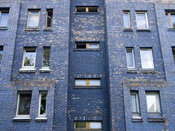 Mavi boyayla boyanmış eski tuğla bina. Bazı yerlerde, kaplama soyulmuş. Bazı pencereler açık, diğerleri kapalı..