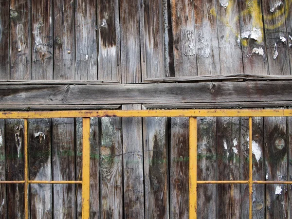 Yanındaki sarı metal çitin yanındaki eski ıslak ahşap duvarın bir parçası..