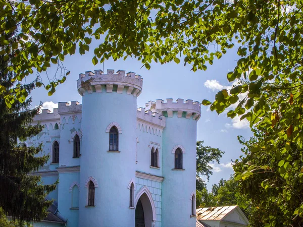 Güneşli bir günde yapraklar ve ağaçlarla çevrili güzel bir peri masalı kalesinin bir parçası. Eski binanın duvarları açık mavi ve beyaza boyandı. Sihirli atmosfer.