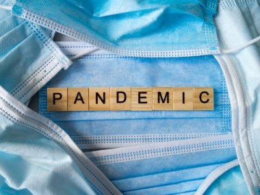 PANDEMIC kelimesi mavi cerrahi maskelerin arka planında ahşap harflerle kaplıydı..