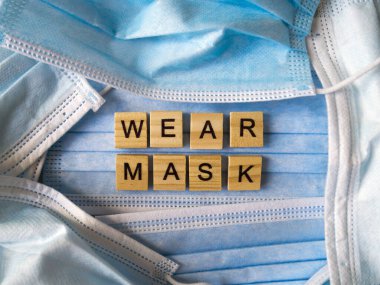 Mavi cerrahi maskelerin arka planında ahşap harflerle kaplanmış sözcükler var..