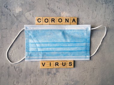 CORONA VIRUS kelimeleri mavi cerrahi maskelerin arka planında ahşap harflerle sıralanmış..