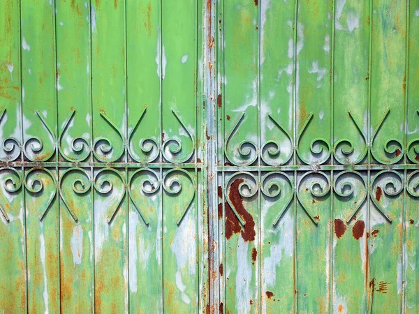 Part of a metallic green fence and gate. Colorful stains of paint and rust on the surface.