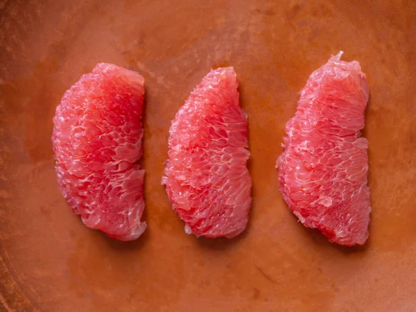 Kahverengi bir tabakta soyulmuş üç greyfurt diliminin üst görüntüsü.