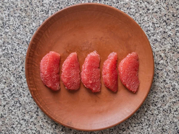 Top view of a clay plate and five pieces of peeled grapefruit.