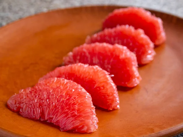 Side view of five pieces of peeled grapefruit on a clay surface.