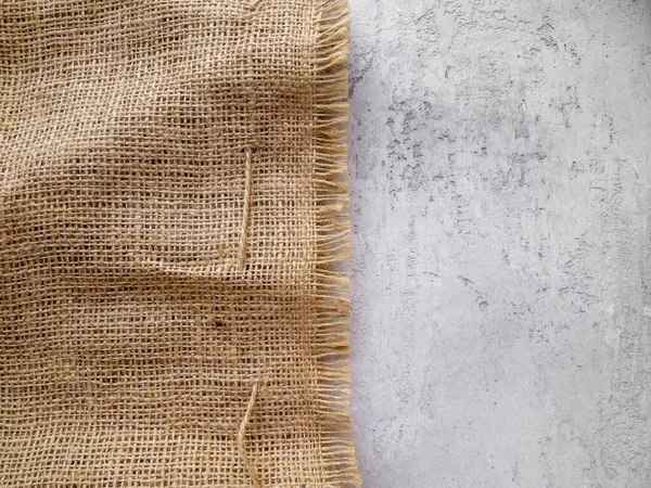 Soyut nötr arkaplan. Bir parçası düz olmayan gri beton, diğer parçası kaba kahverengi çuval bezi..