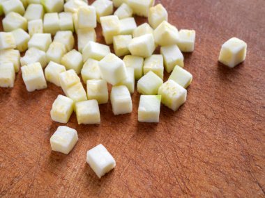 Kahverengi ahşap bir tahta üzerinde Brunoise kabağı. Kabak küçük küp şeklinde kesilmiş..