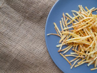 Yarım tabak klasik kızarmış patatesin üst görüntüsü. Sert, sade masa örtüsü..