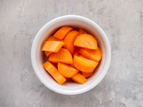 Beyaz bir kâse ve doğranmış havuç manzarası. Paysanne kesimi.