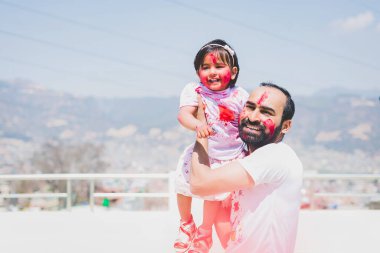 Father and daughter having fun during Holi Purnima or Holi festival after applying colors to each other. Festival of colors celebration. Family fun, family celebration.Hindu Festival. 