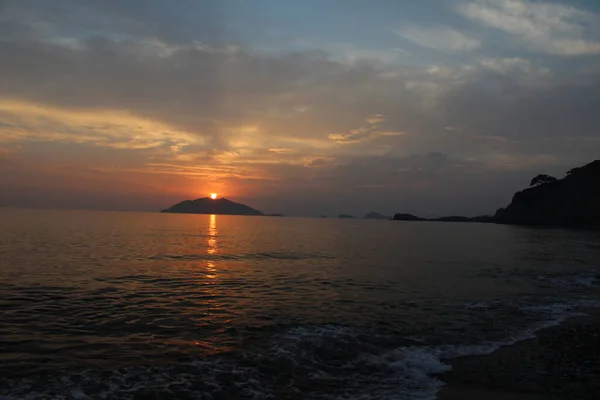 Renkli bulutlar, mavi gökyüzü, günbatımı, deniz ve ada siluetleri.